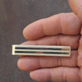 Gold tone striped tie bar clip held in hand, front close-up view