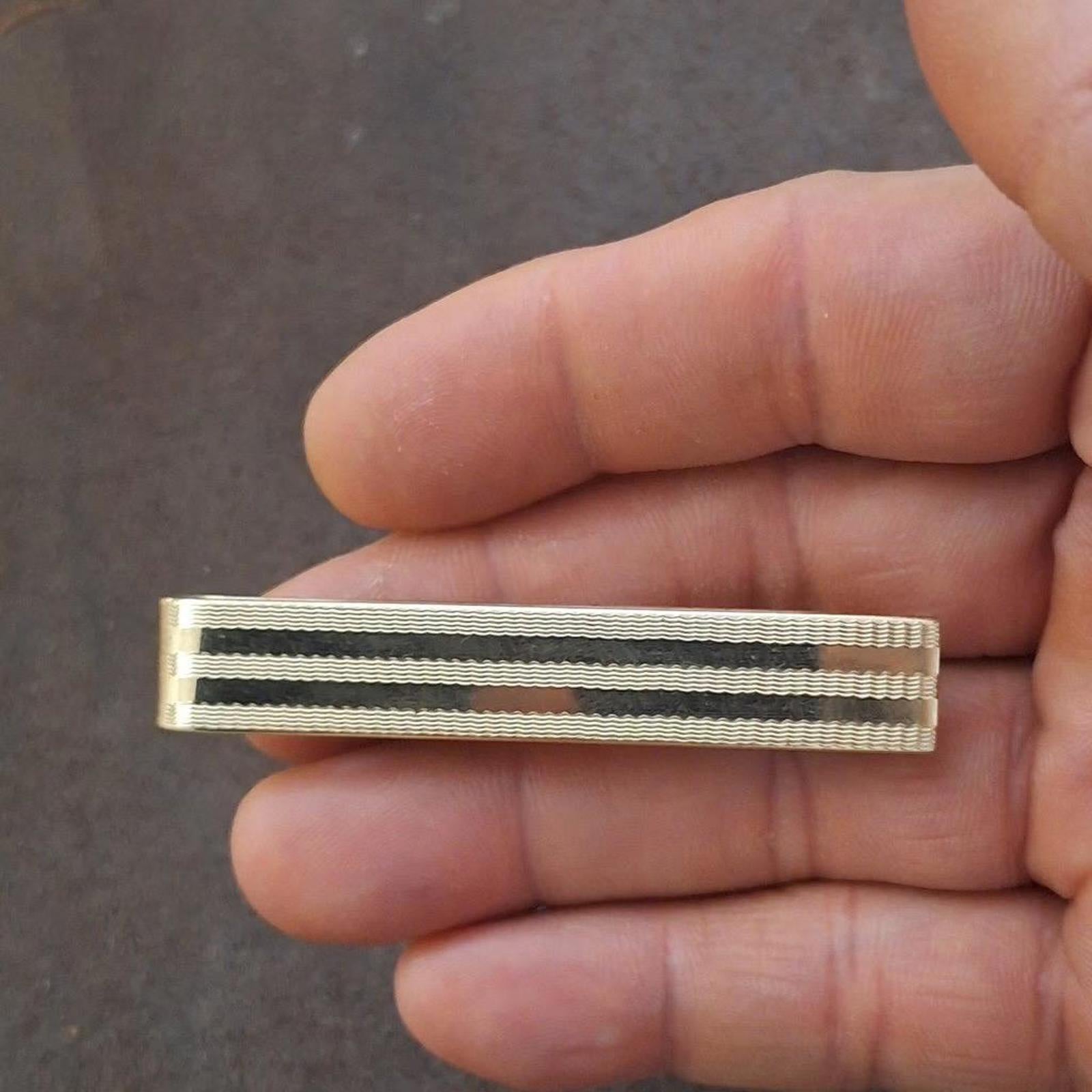 Gold tone striped tie bar clip held in hand, front close-up view