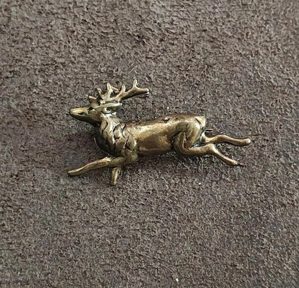 Brass running deer figurine lying on textured gray surface, side view
