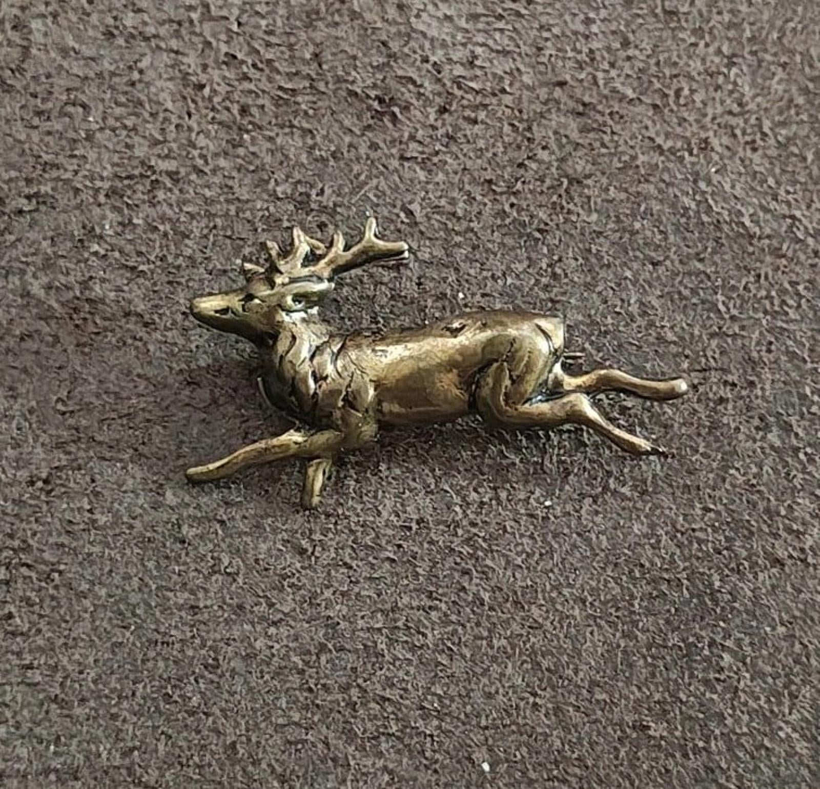 Brass running deer figurine lying on textured gray surface, side view