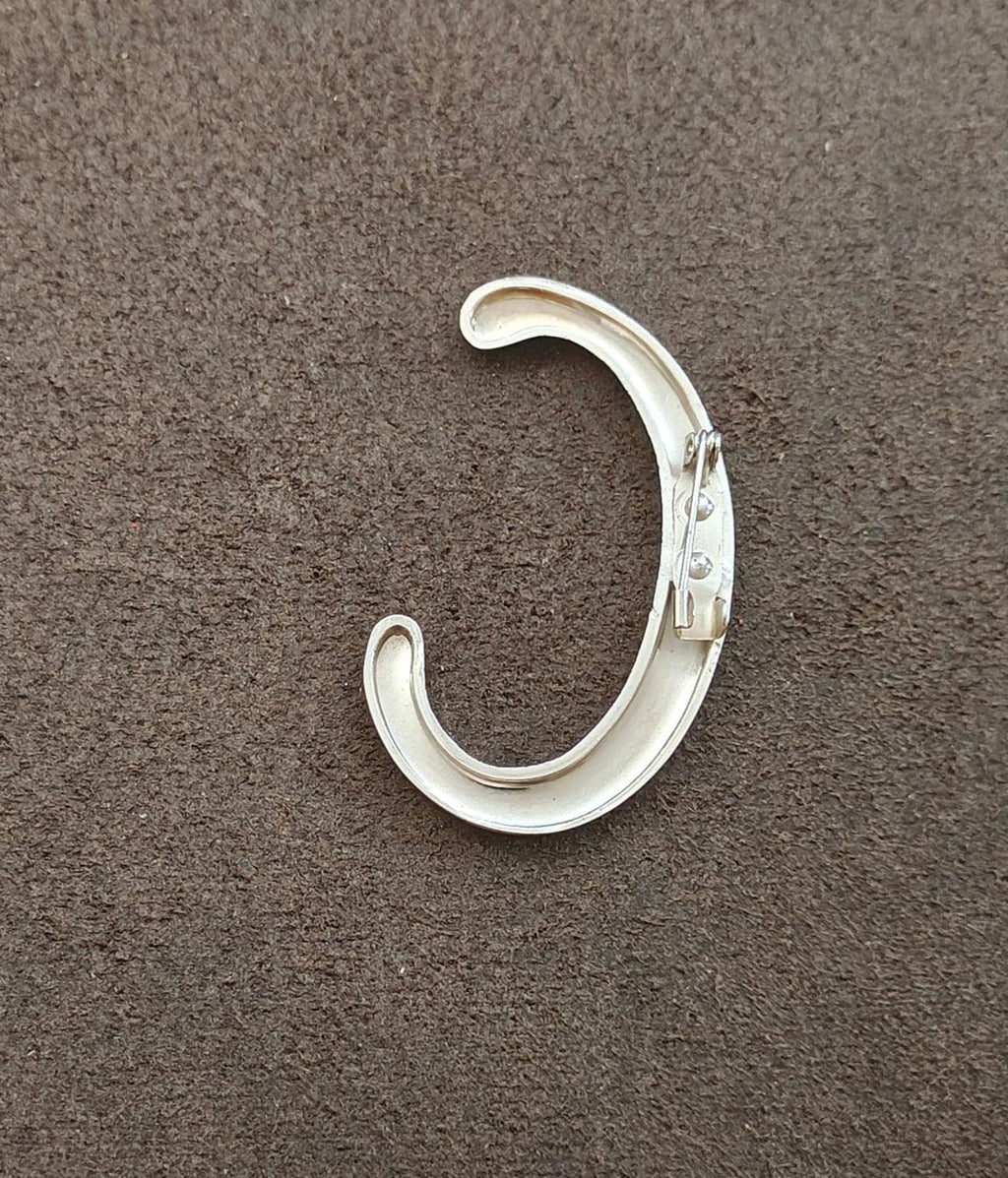 Silver tone letter C monogram pin/brooch with backing clasp/fastener shown on surface.