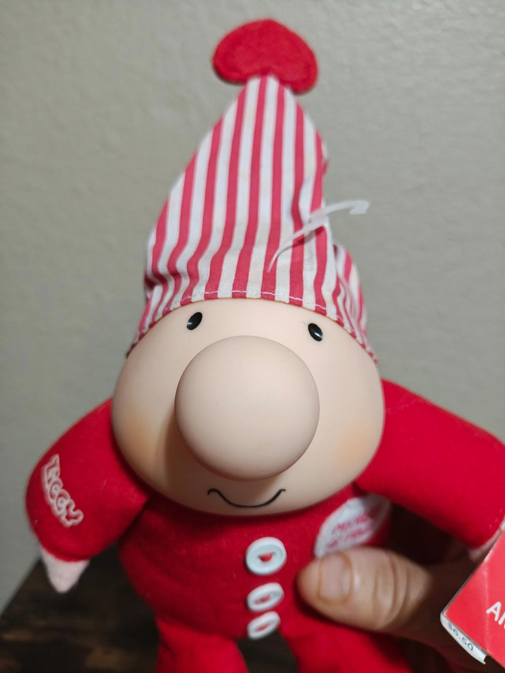 Red plush character with a red-and-white striped heart hat and smiling face, close-up