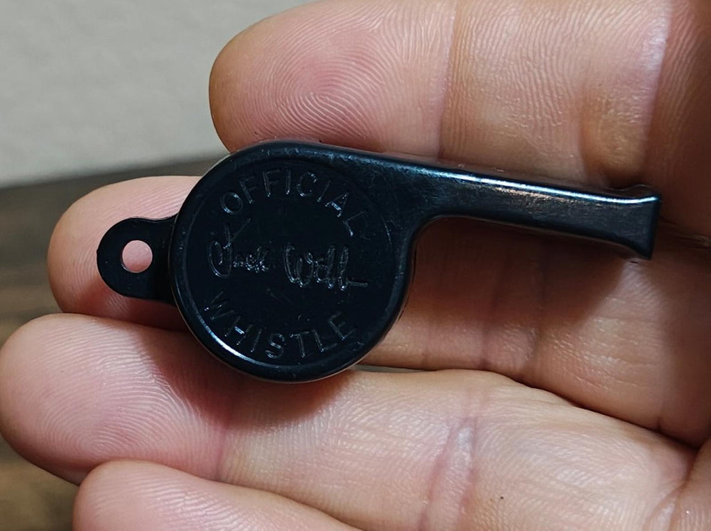Black whistle end with engraved face and loop, held in fingertips.