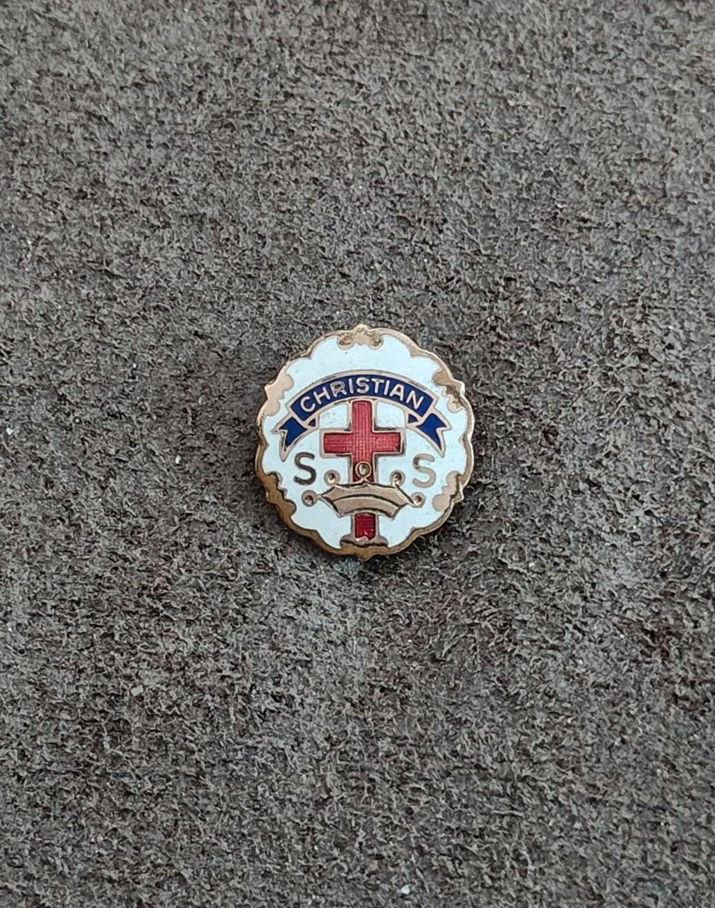 Round Christian enamel pin on dark fabric, gold edge, red cross and blue “CHRISTIAN”