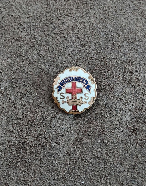Round Christian enamel pin on dark fabric, gold edge, red cross and blue “CHRISTIAN”