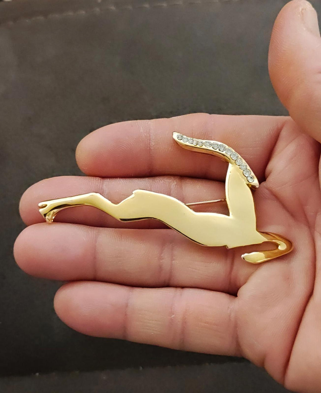 Gold-tone leaping gazelle/impala brooch with rhinestone trim, held in hand