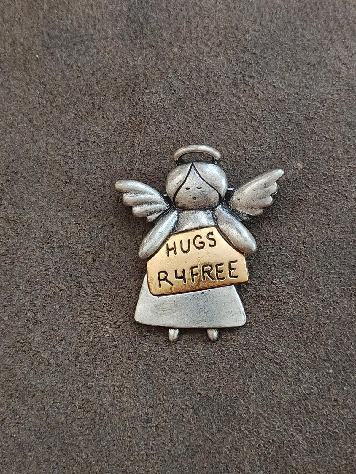 Silver angel brooch standing figure with wings; text panel says HUGS R4FREE
