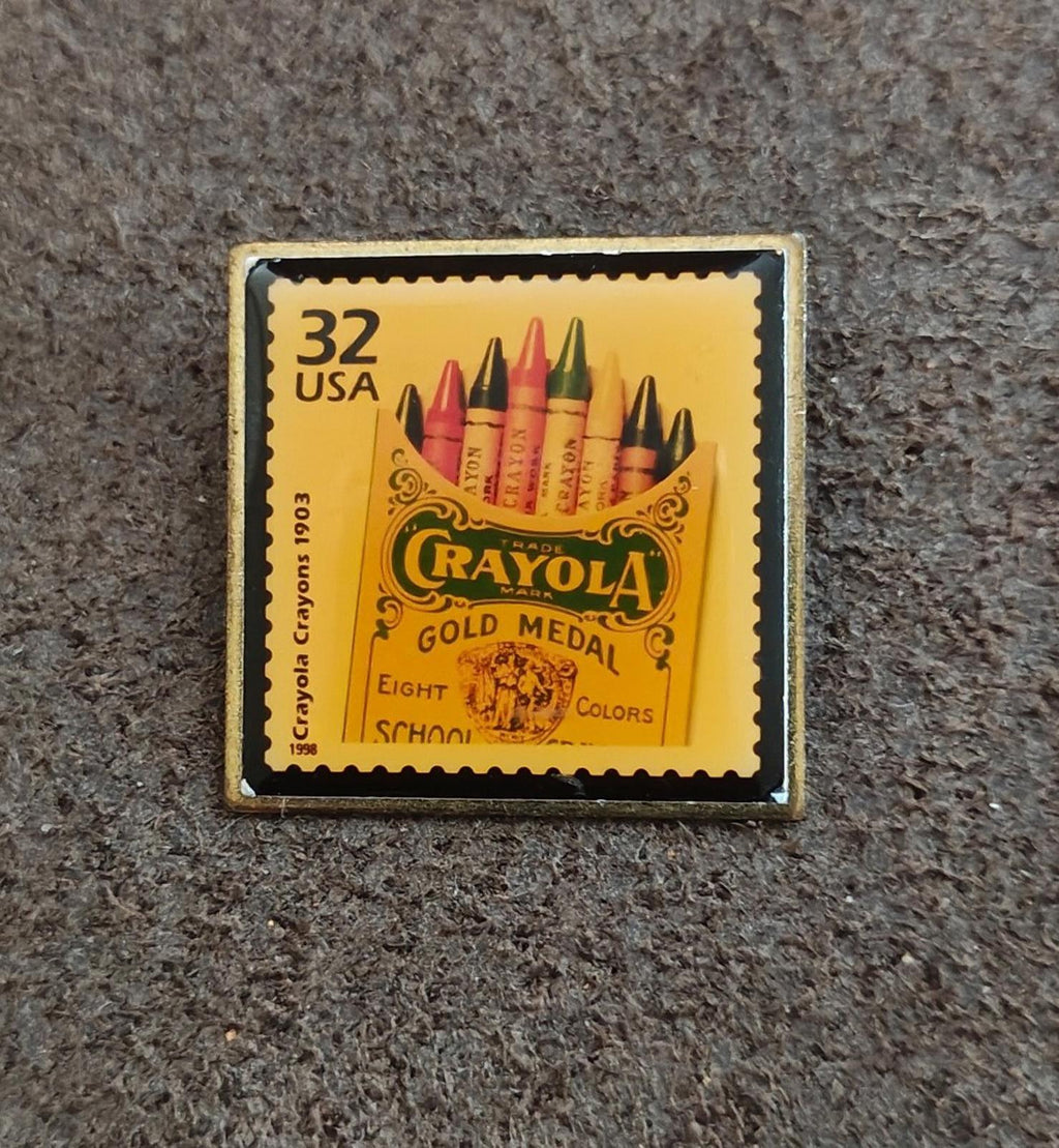 Square gold-tone pin with “32 USA” stamp artwork and Crayola Gold Medal lettering