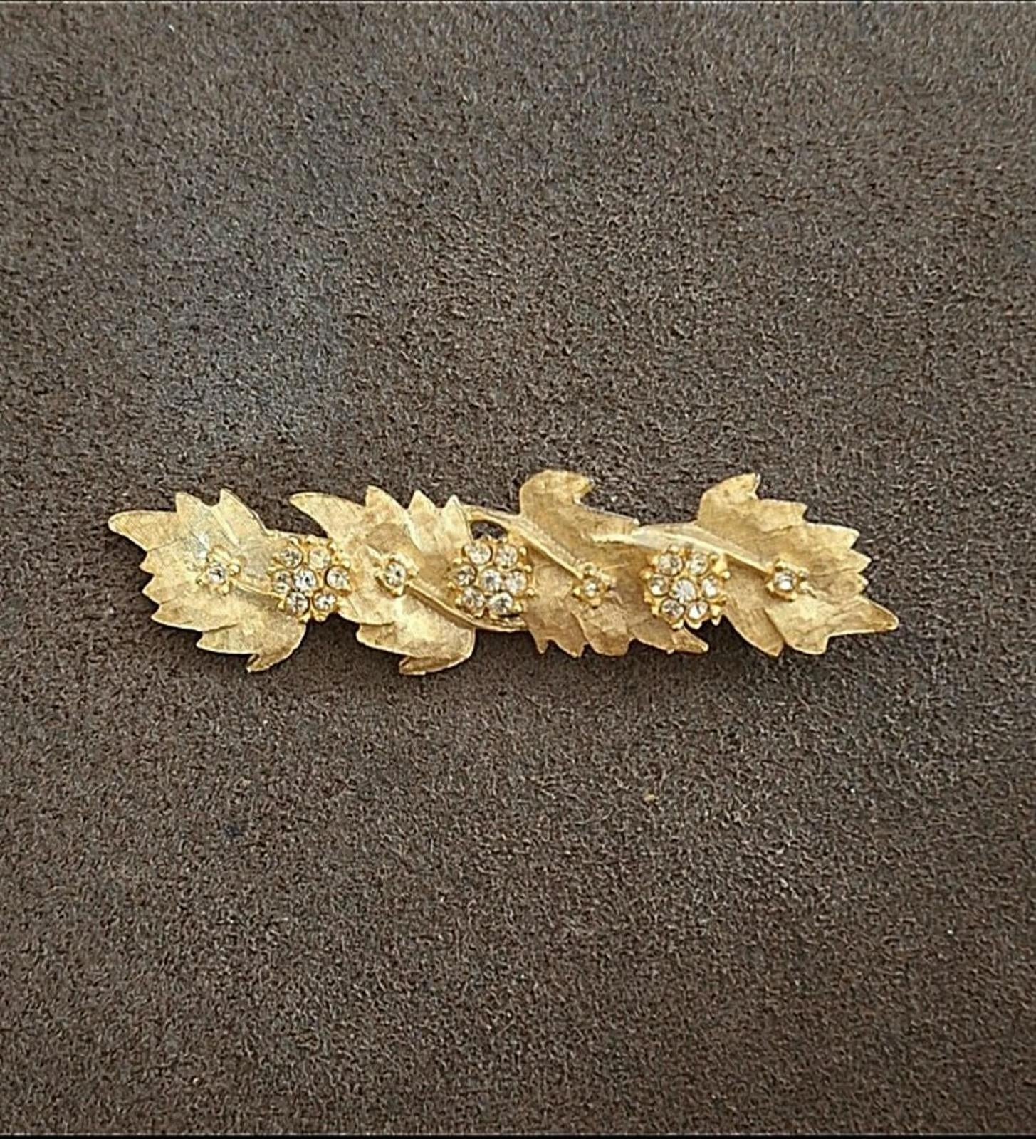 Gold tone leaf and flower rhinestone brooch pin on dark fabric background