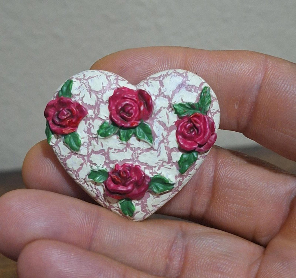 Heart-shaped resin pin close-up: crackled white heart with red roses and green leaves