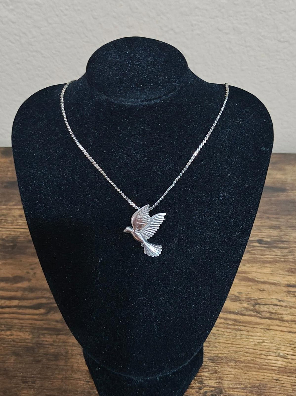 Silver-tone dove pendant necklace on a black bust display