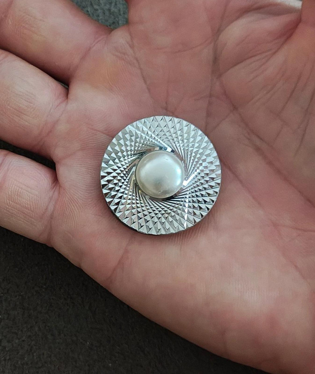 Round silver-tone scarf clip held in hand; textured disc with faux pearl front
