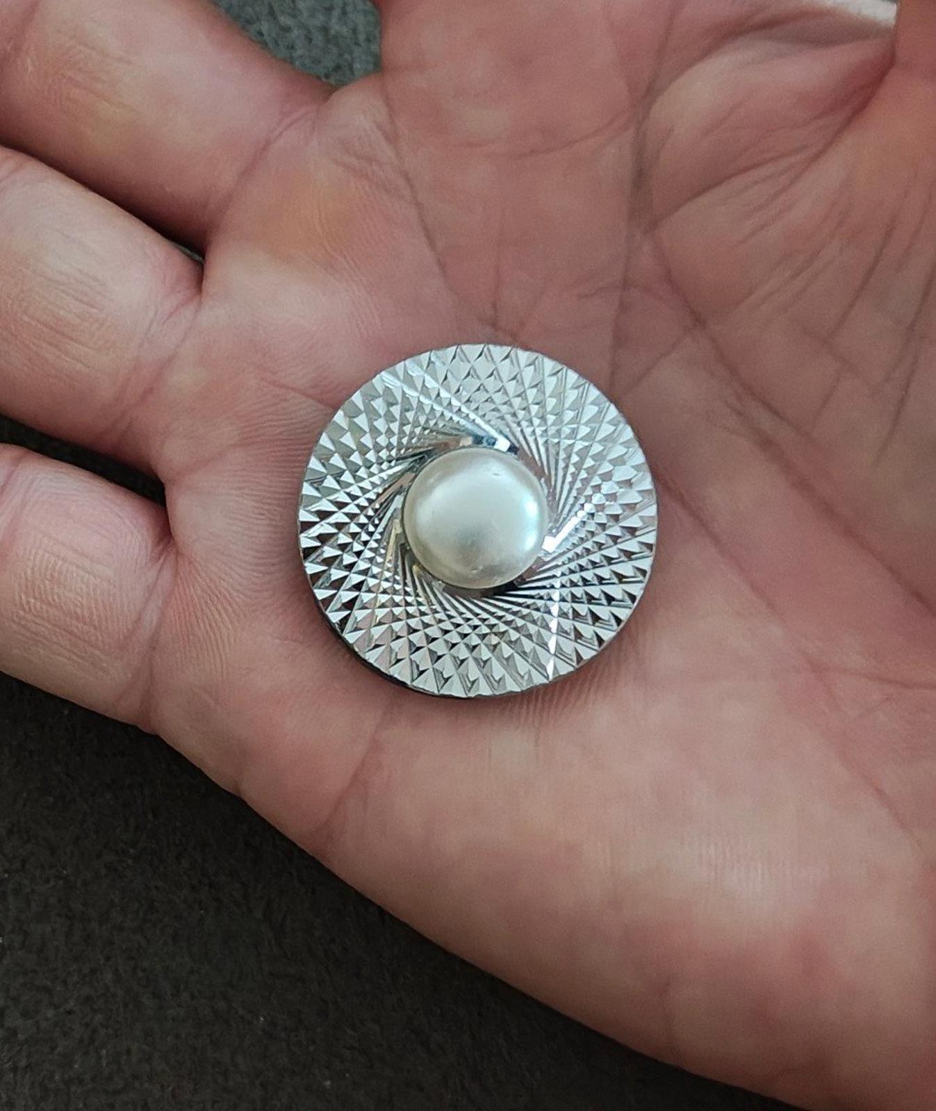 Round silver-tone scarf clip held in hand; textured disc with faux pearl front