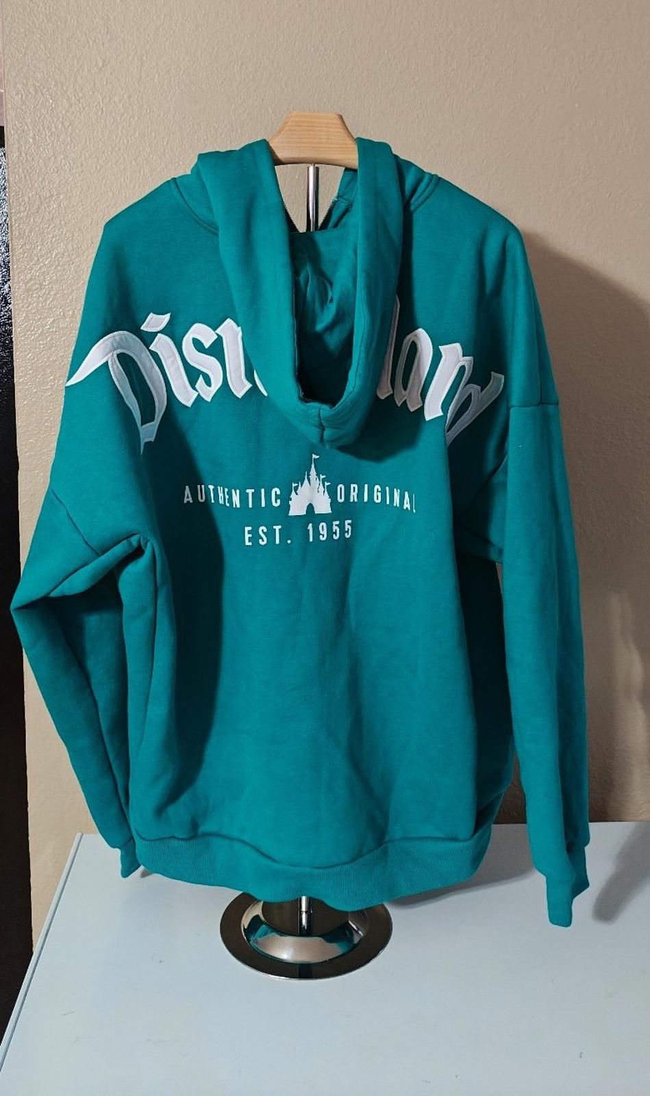 Teal zip-up hoodie with large white “Disney” lettering and “Est. 1955” on front