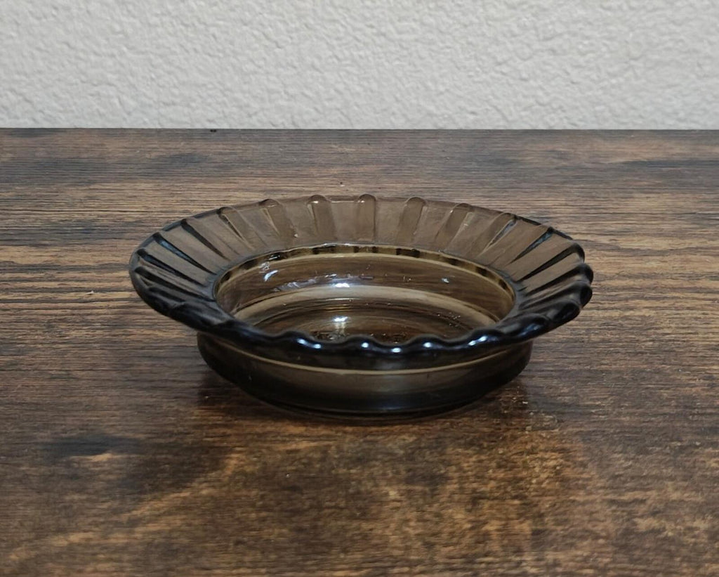Clear ribbed glass ashtray with dark tint, shallow bowl shape