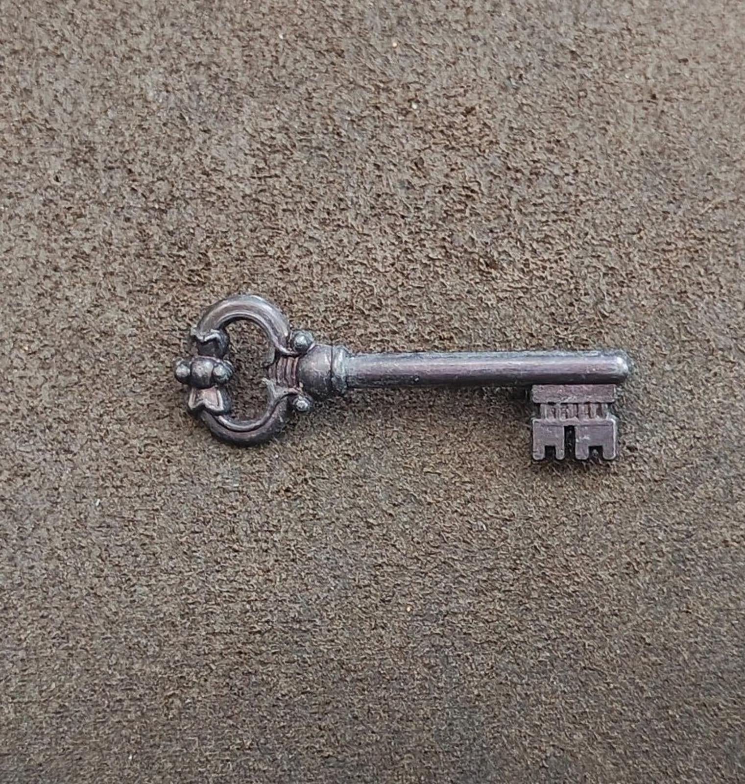 Pewter skeleton key brooch lying flat, round bow and ornate teeth detail