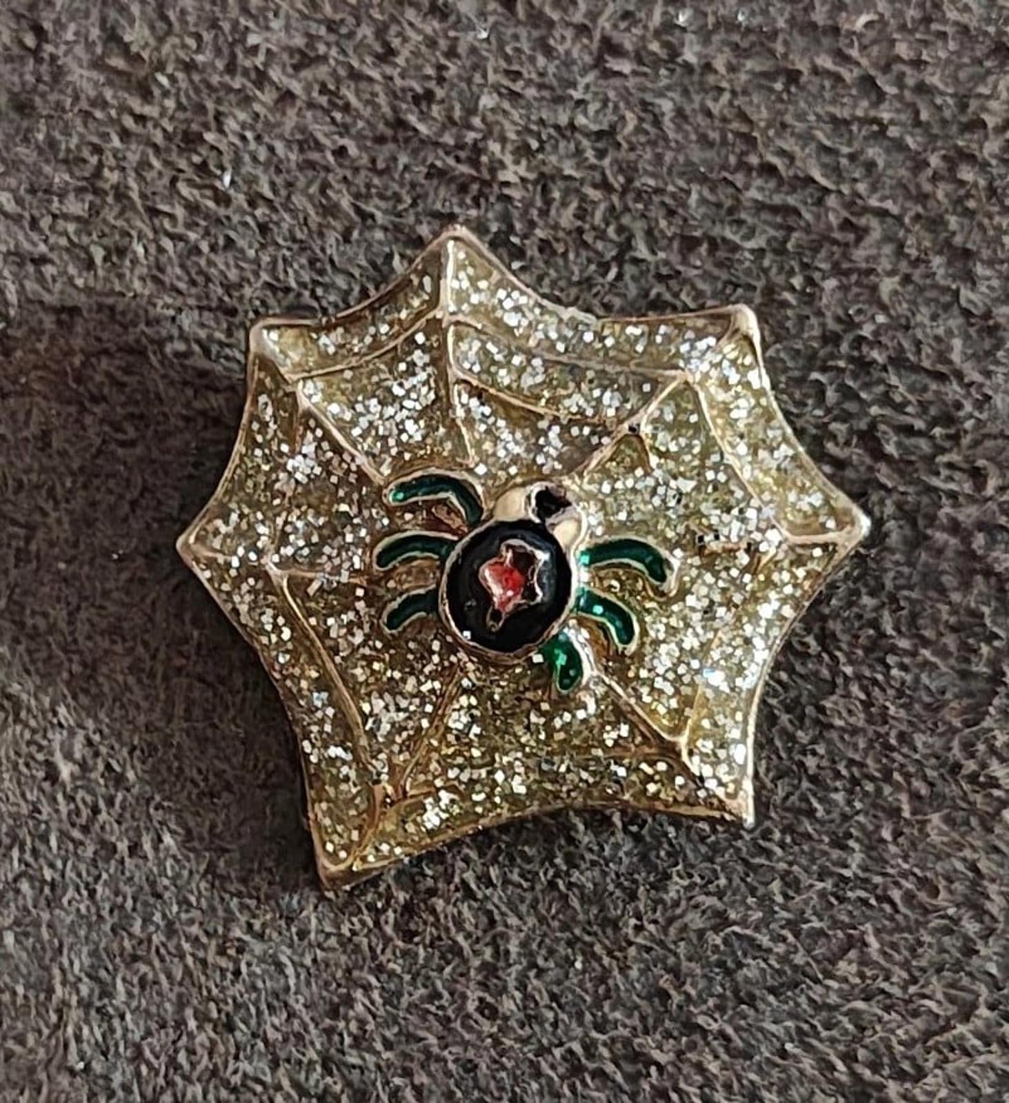 Gold spider web enamel pin with sparkle texture, black spider body, red center, green legs