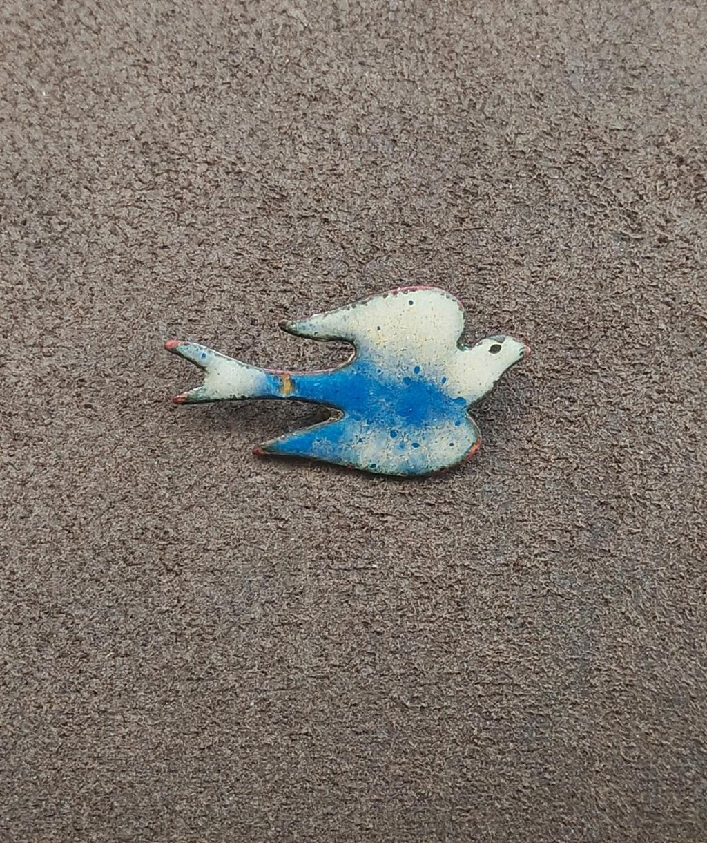 Blue and white enamel bird brooch lying flat, speckled details on body
