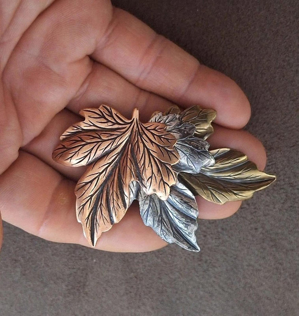 Layered leaf pin brooch with brown, gold, and silver leaves, held close to camera