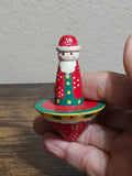 Santa spinning top toy held in hand, face with white beard, red suit and green base