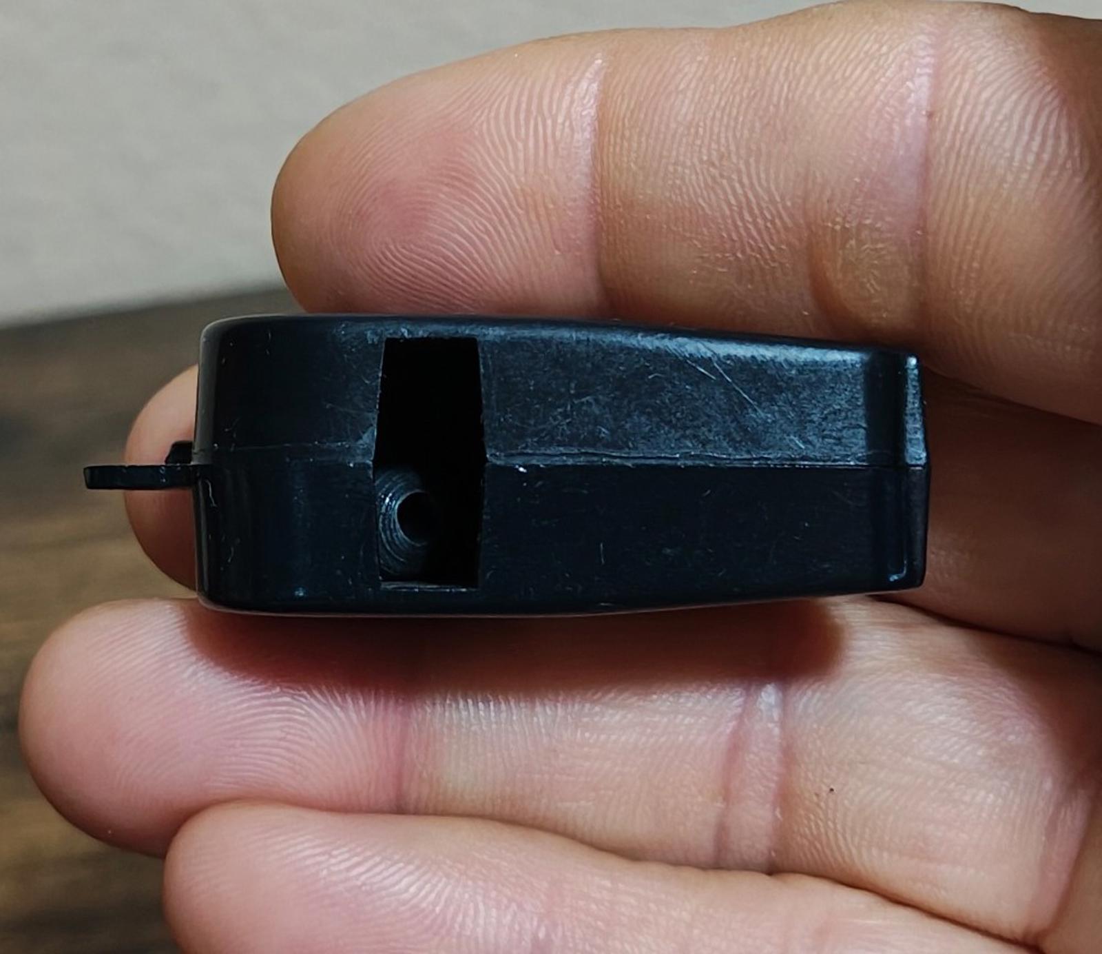 Black whistle body with loop mount, side view held in fingertips.