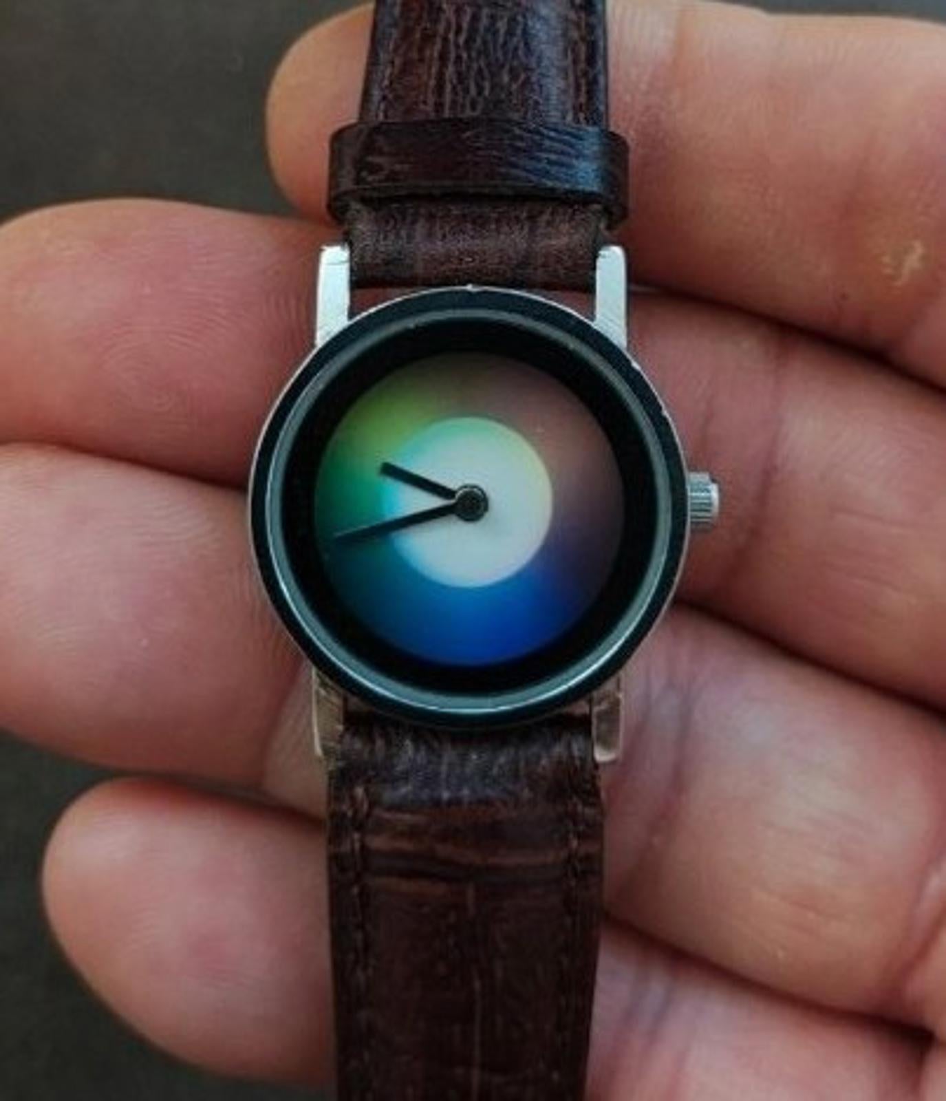 Round dial wristwatch with iridescent blue-green face, black bezel, brown leather strap