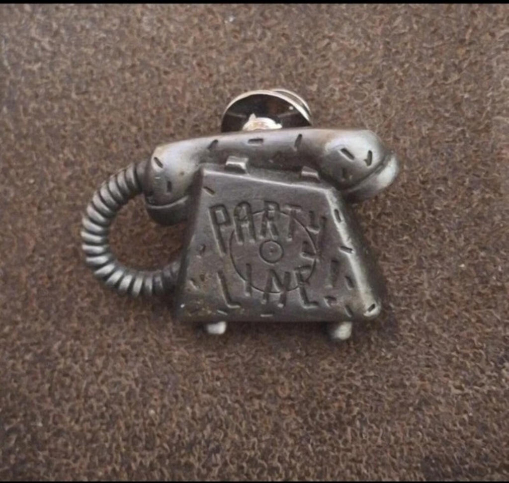 Silver telephone-shaped novelty pin with 'PARTY LINE' lettering, handset detail, and cord