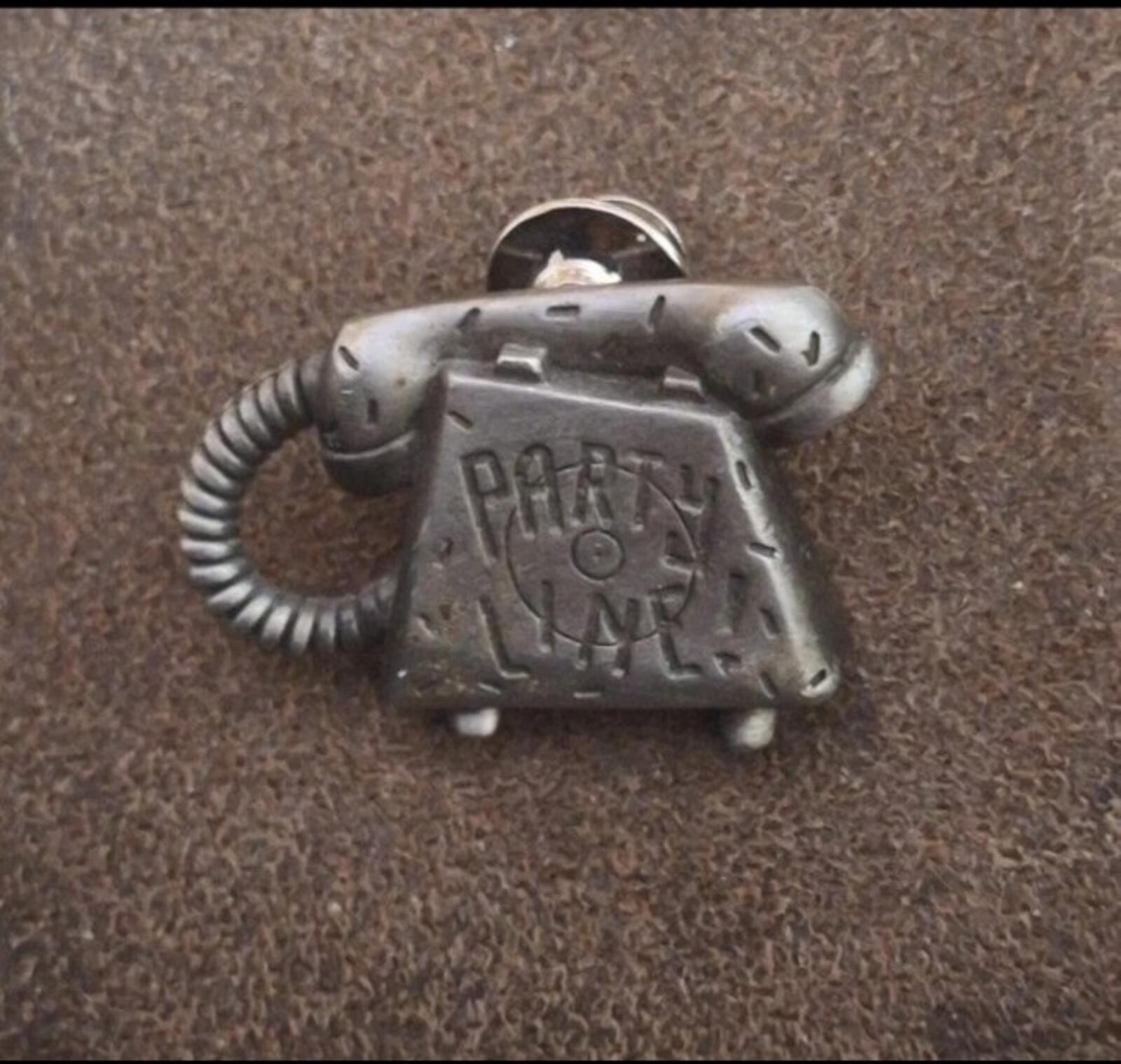 Silver telephone-shaped novelty pin with 'PARTY LINE' lettering, handset detail, and cord