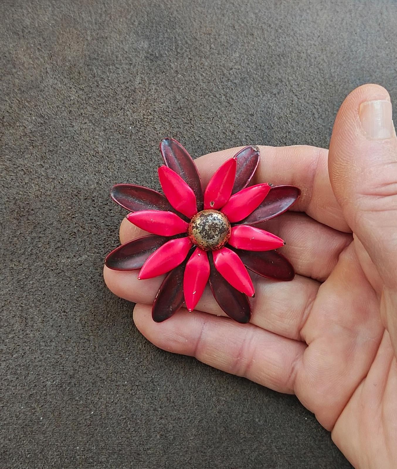 Red and burgundy flower enamel pin brooch held in fingers, centered front view