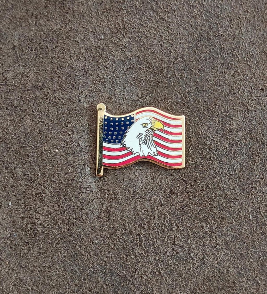 Gold-tone enamel wavy American flag lapel pin with bald eagle, shown on gray fabric
