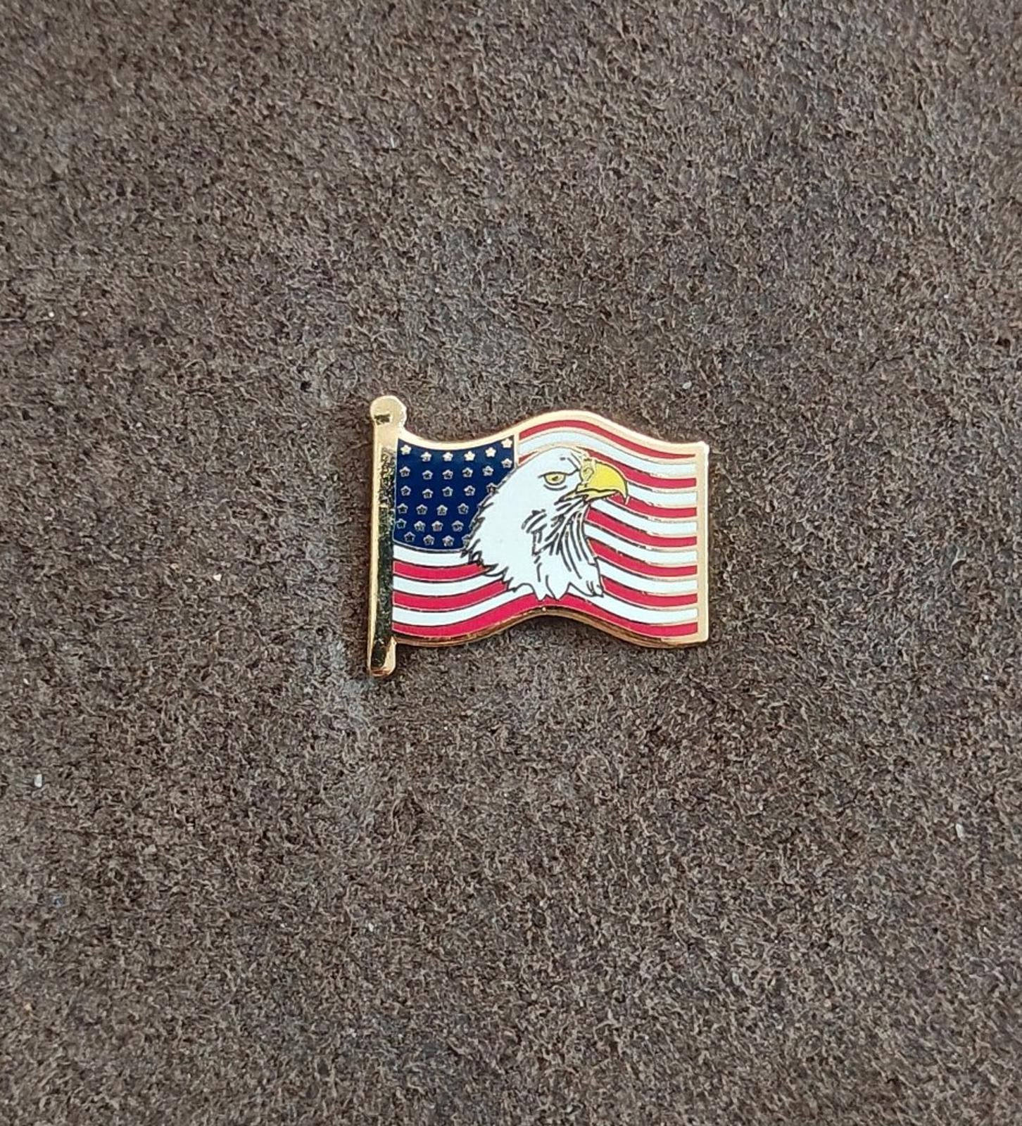 Gold-tone enamel wavy American flag lapel pin with bald eagle, shown on gray fabric