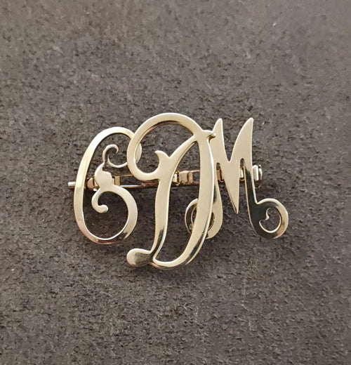 Gold-tone monogram brooch pin showing red enamel letters E, D, M from a side angle