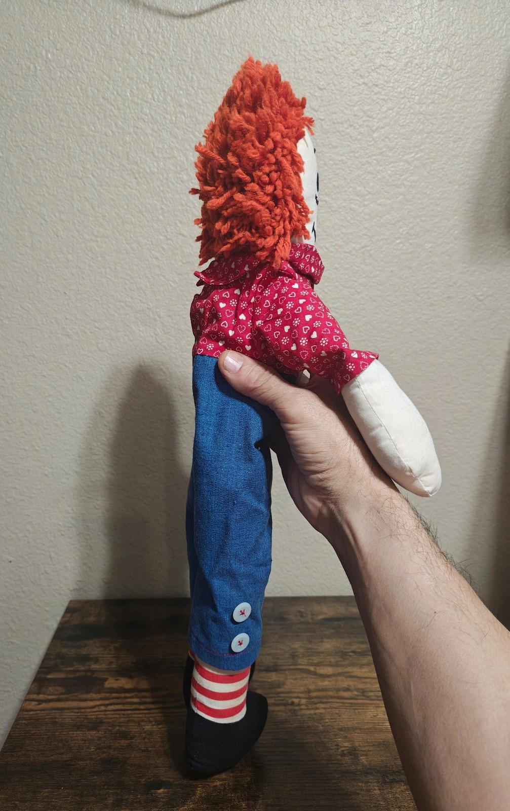 Handmade rag doll side view with orange yarn hair, red heart-pattern shirt, blue overalls, socks.