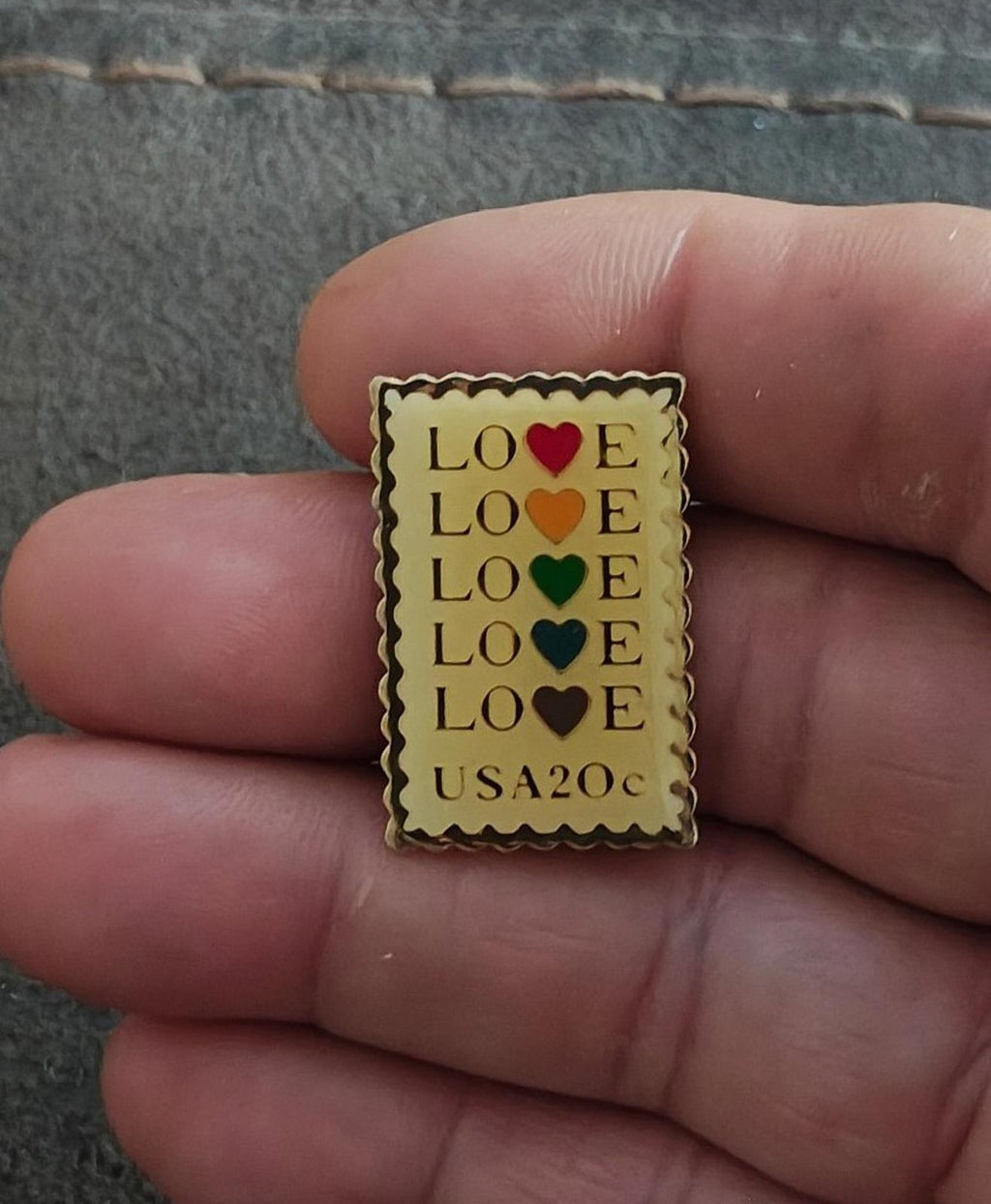 Small gold-tone enamel stamp pin with “LOVE” and colored hearts, “USA20c” at the bottom.