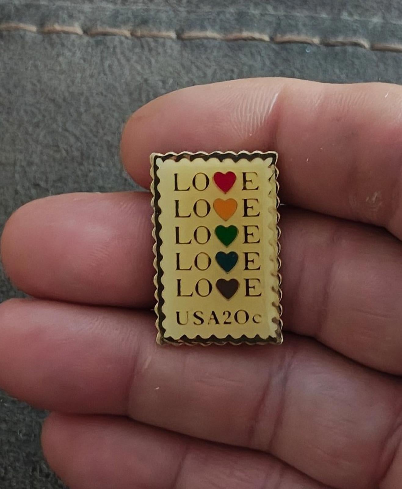 Small gold-tone enamel stamp pin with “LOVE” and colored hearts, “USA20c” at the bottom.