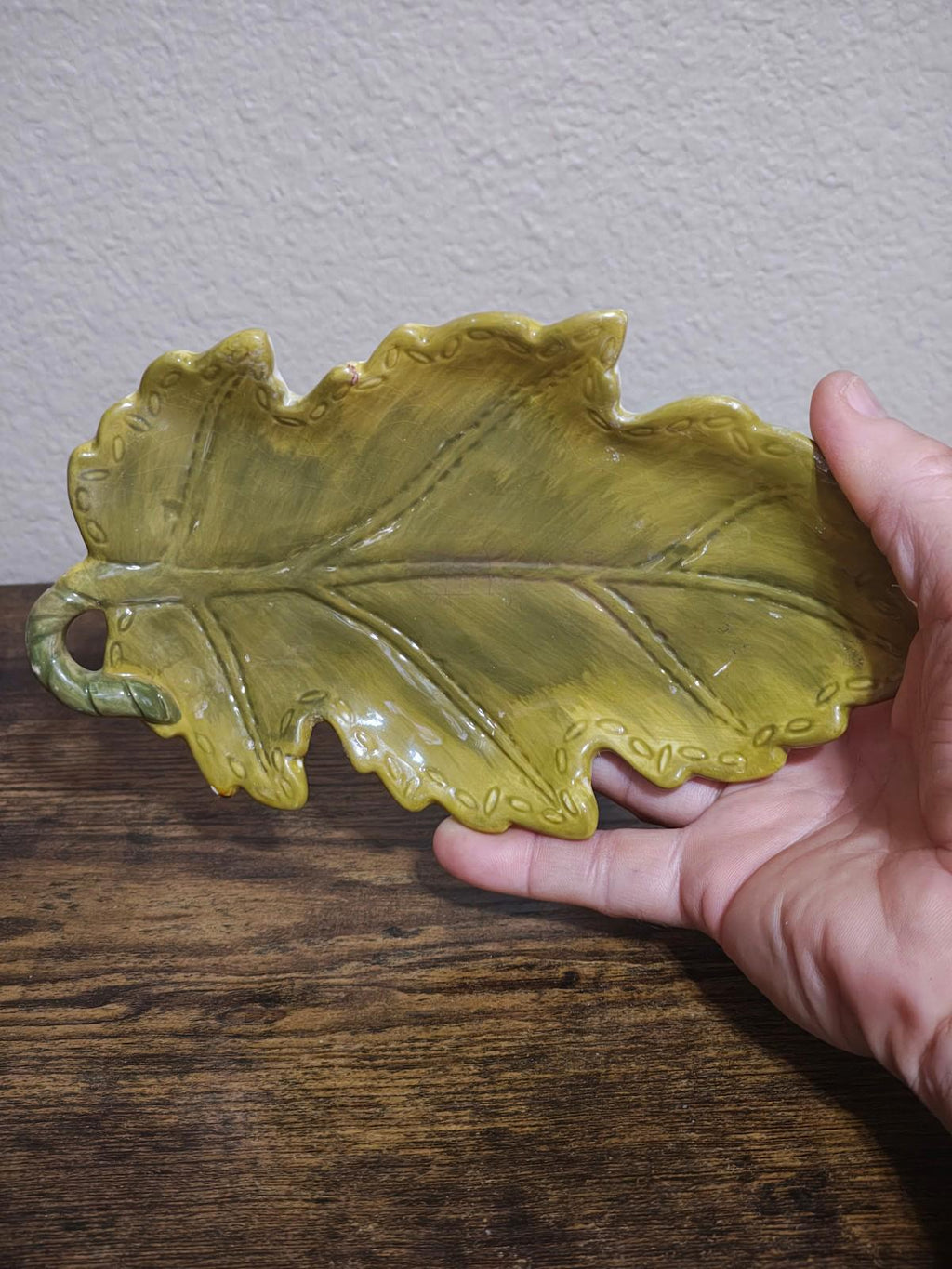 Yellow glazed ceramic leaf dish held from side, showing leaf shape and raised veins.