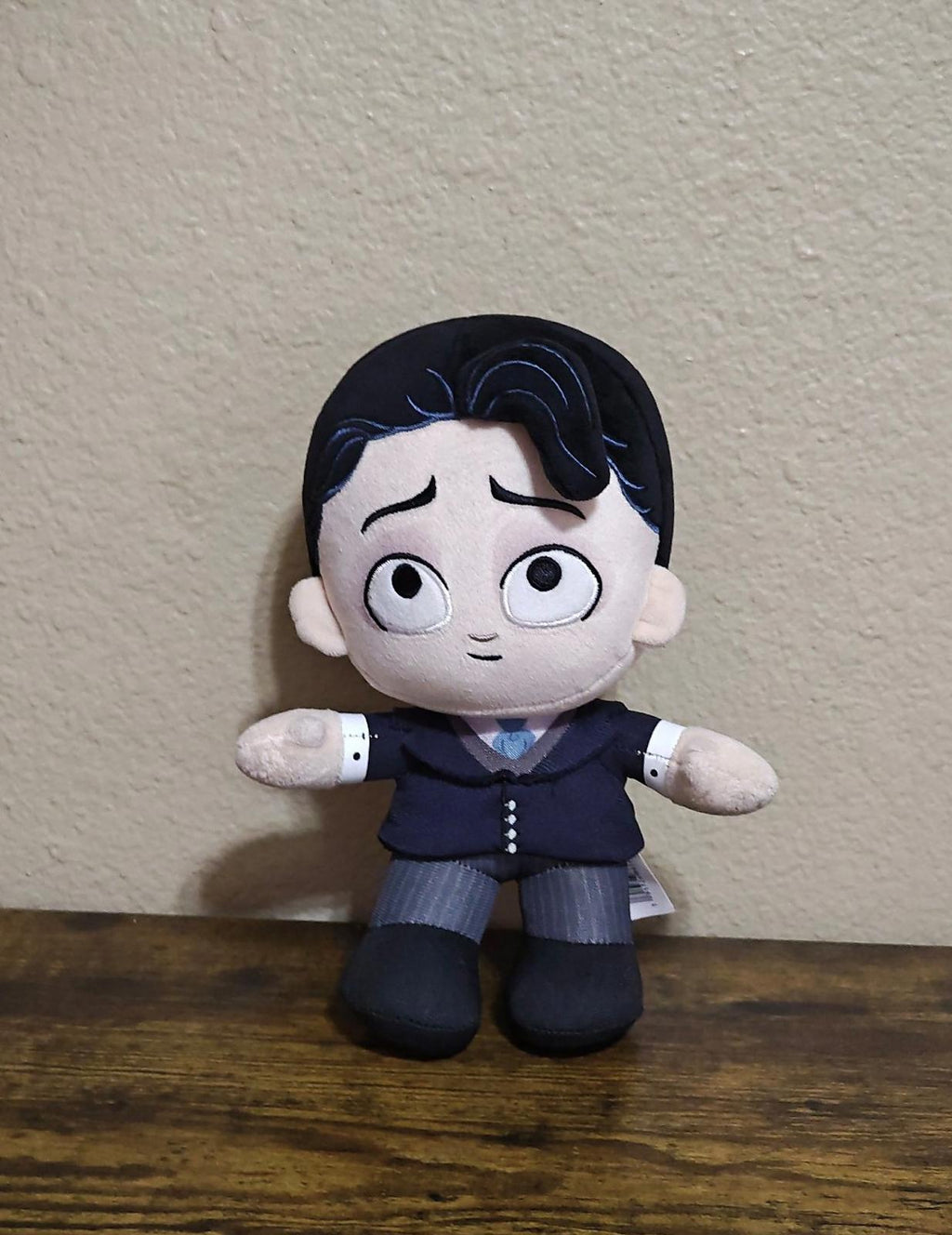 Black plush doll with eyes closed, dark blue outfit and gray striped pants