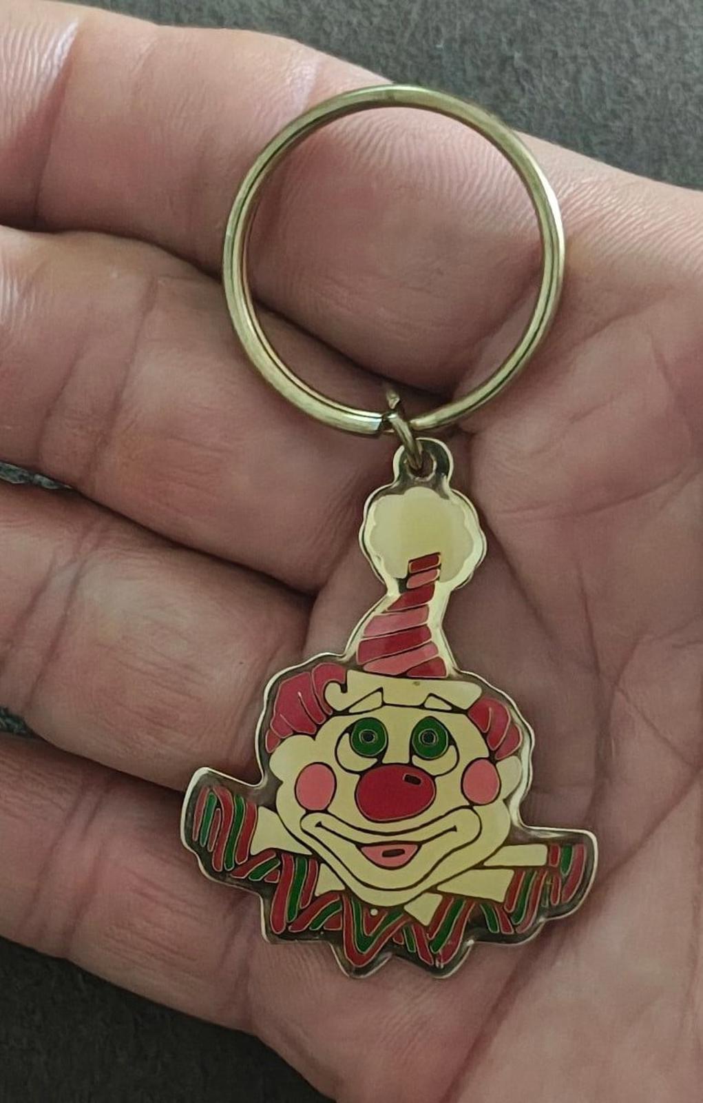 Gold-tone ring keychain with colorful clown face charm, held in a hand