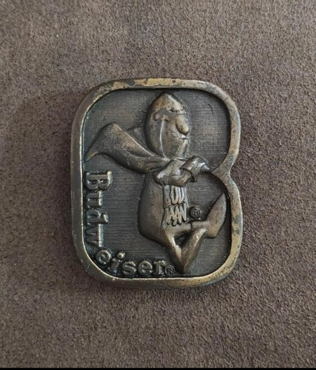 Vintage brass belt buckle front with character in a shield and Budweiser-themed details.