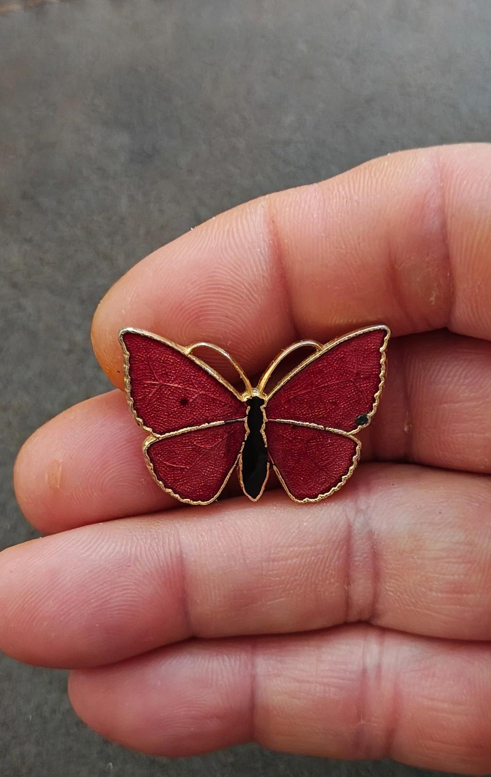 Red butterfly enamel brooch with gold-tone outline and black body, close-up in hand.