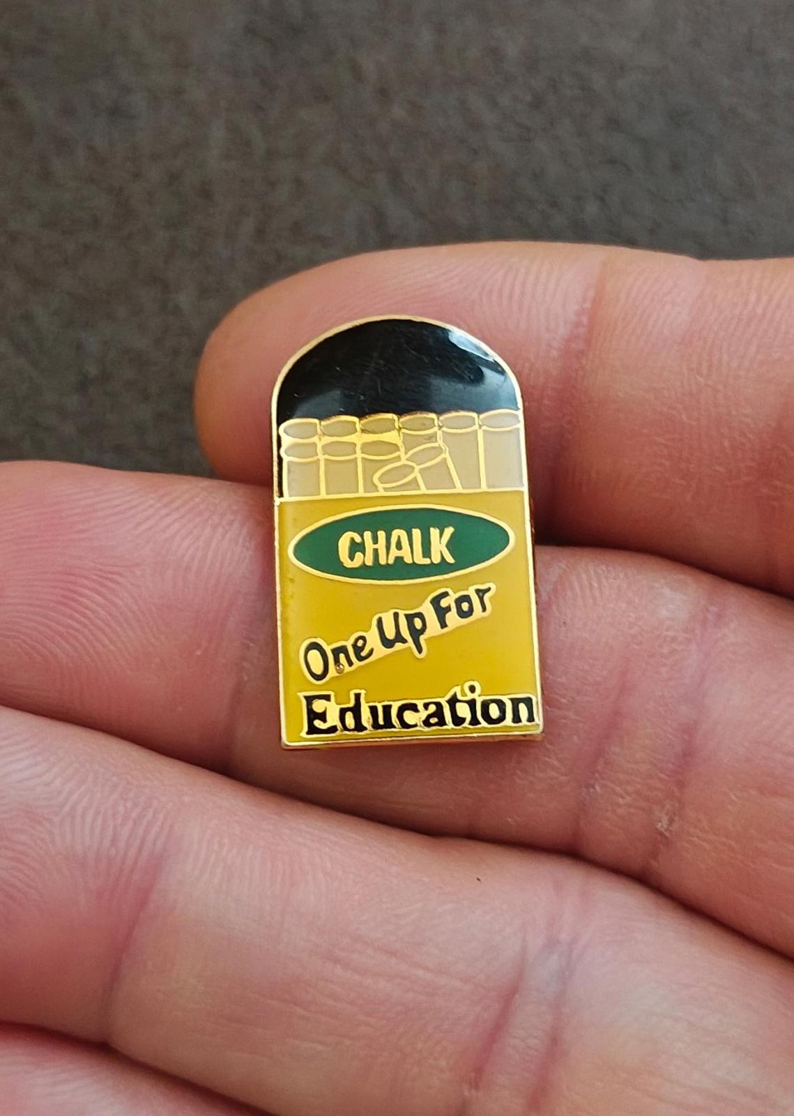 Gold-tone enamel teacher pin front on hand, glossy black top and chalkboard message
