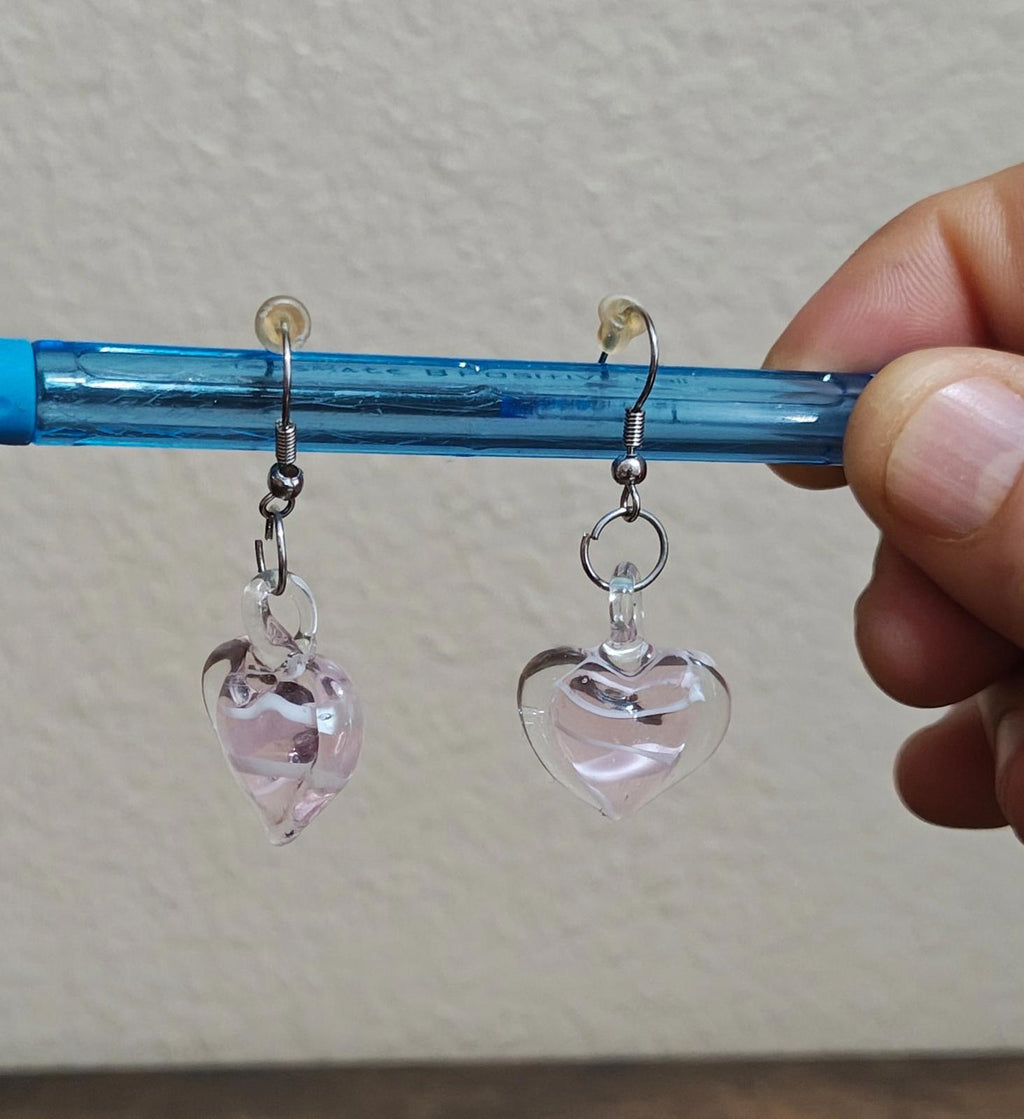 Heart-shaped glass earrings on blue rod; left heart has faint pink color, right is clear.