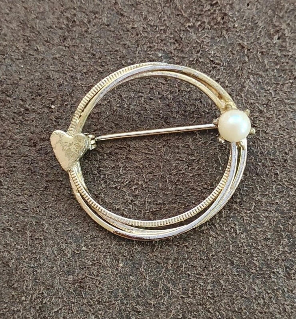 Gold-tone circular eternity brooch showing textured edge and pearl bead on pin