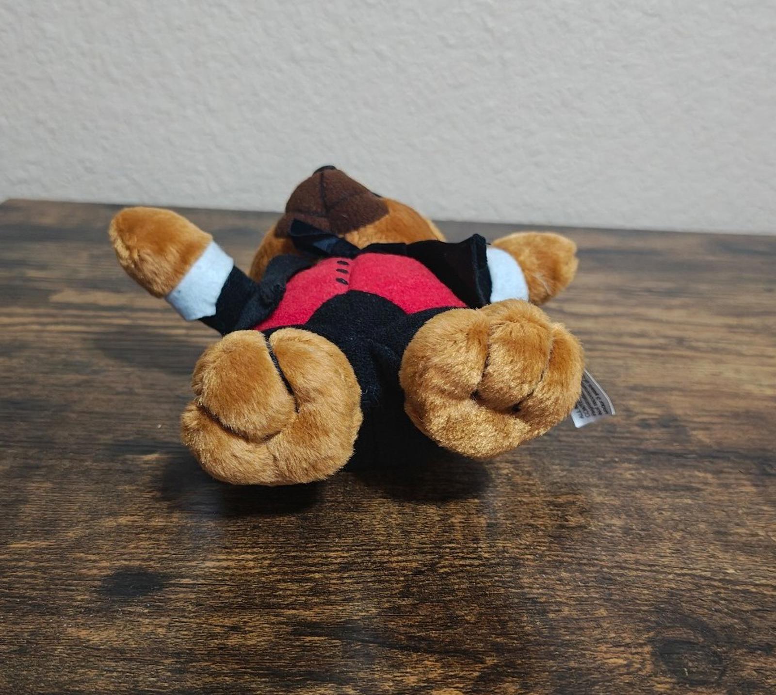 Lying plush bear in black tuxedo with red vest and top hat, showing side profile.
