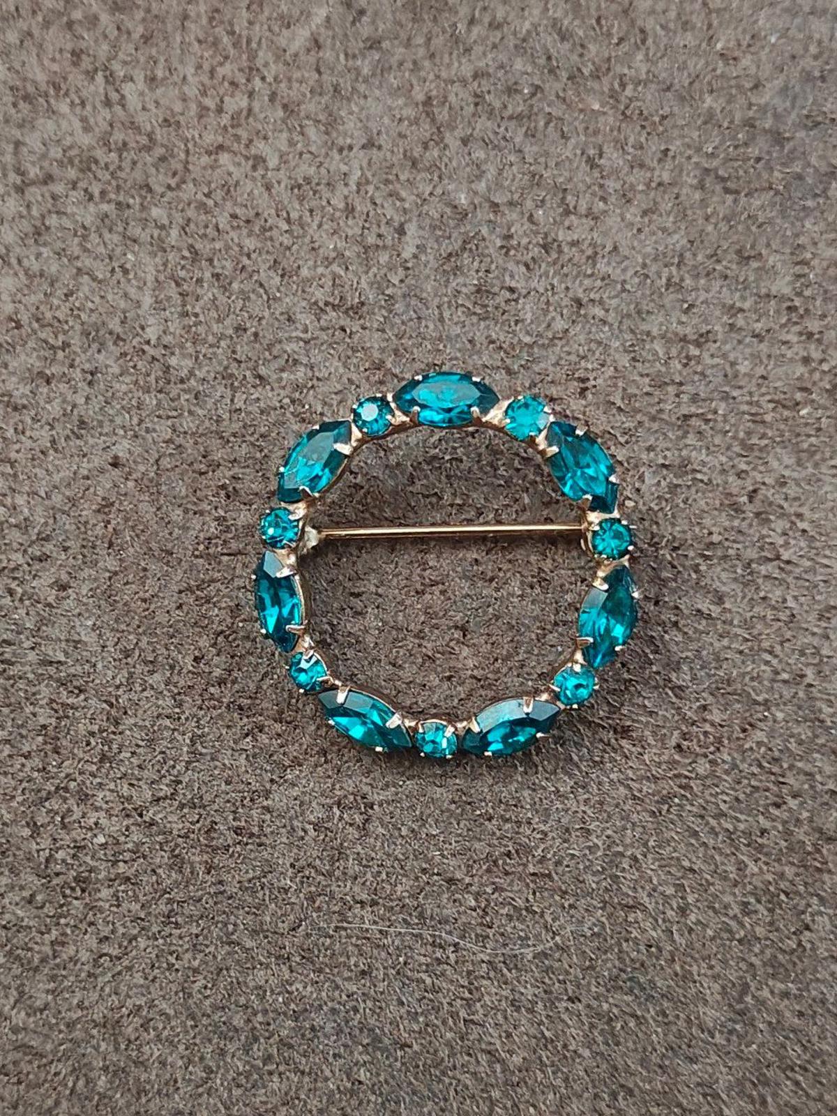 Aqua blue rhinestone round brooch pin on stone-textured background, gold-tone bar