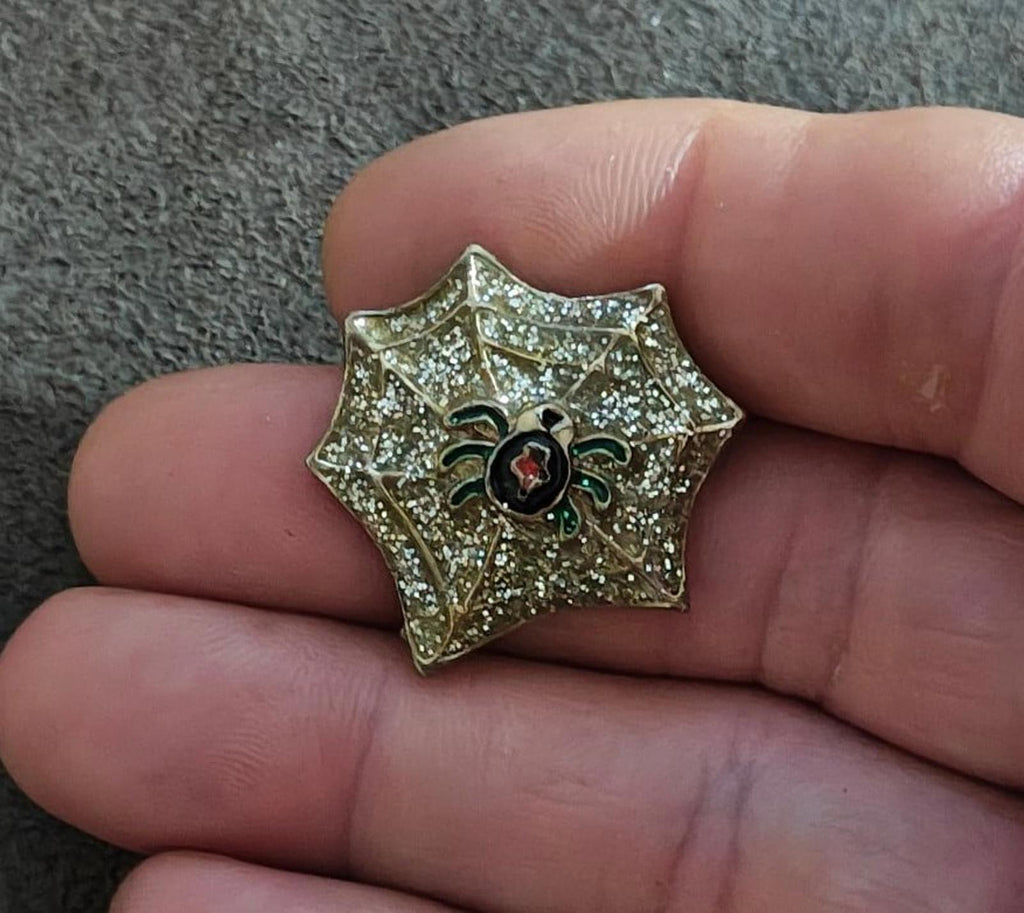 Gold spider web enamel pin in hand, glitter sparkle, black spider with red center and green legs