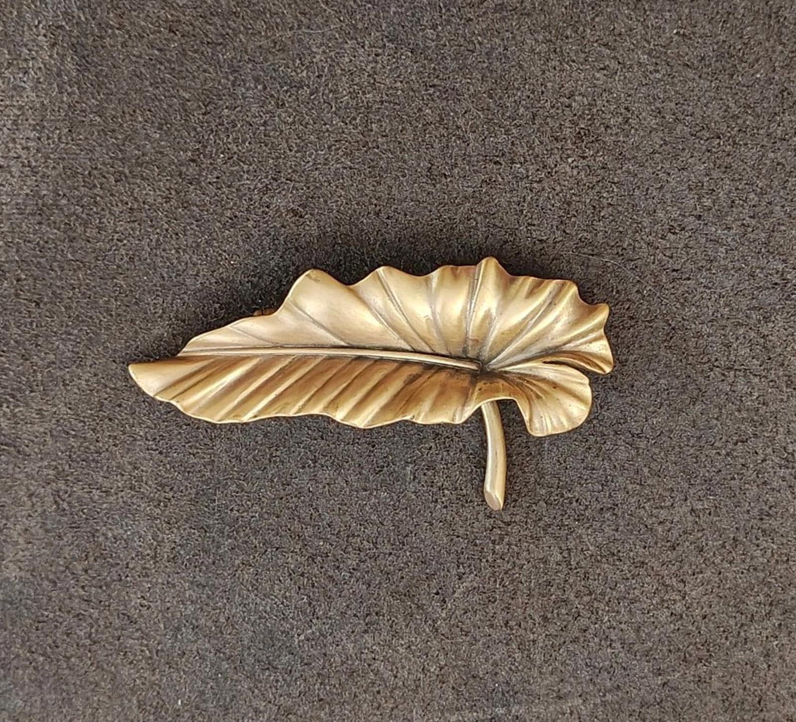 Gold-tone leaf brooch pin with embossed vein details and pin stem visible.