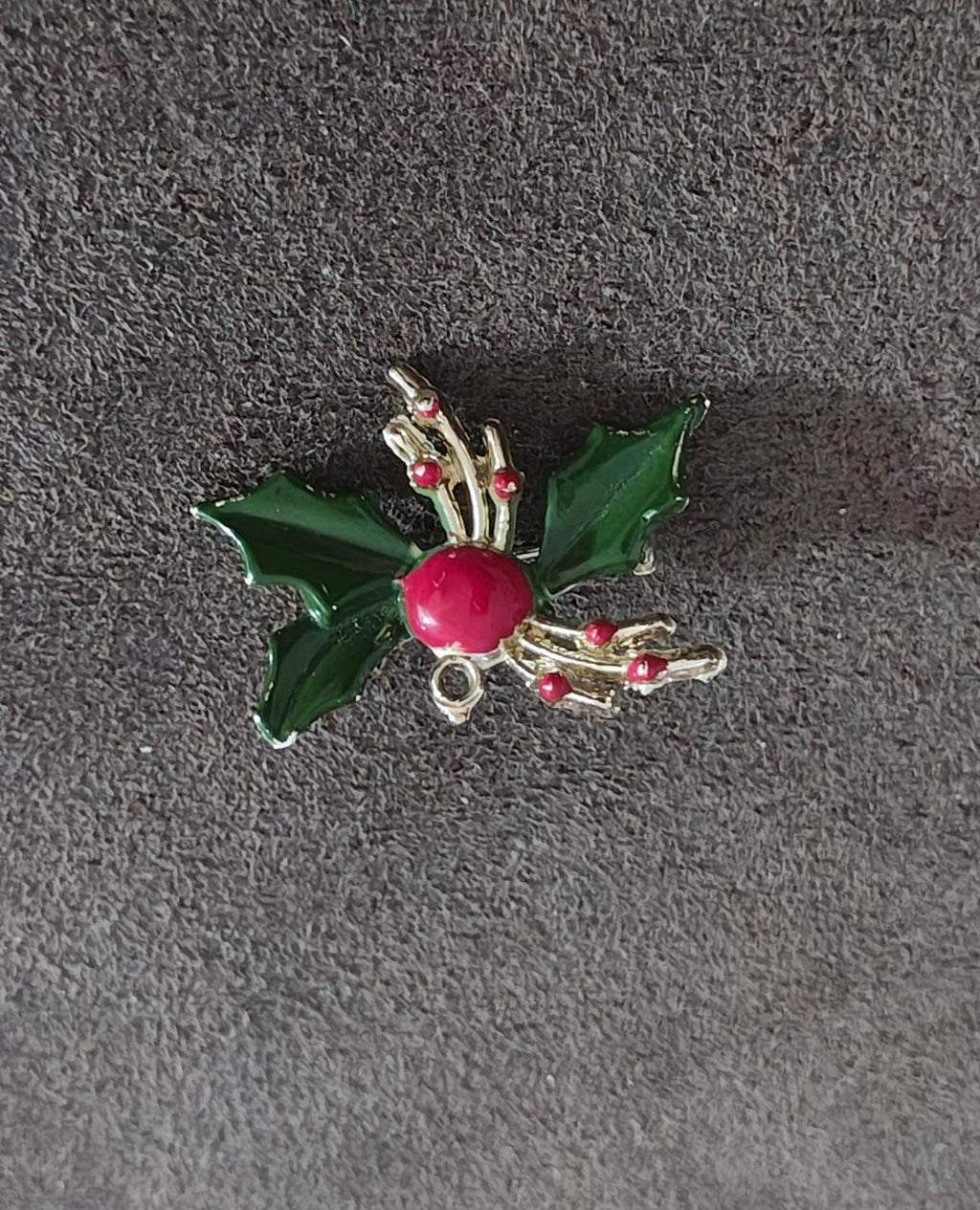 Holly enamel brooch pin on dark fabric: green leaves, red berry center, gold-tone details