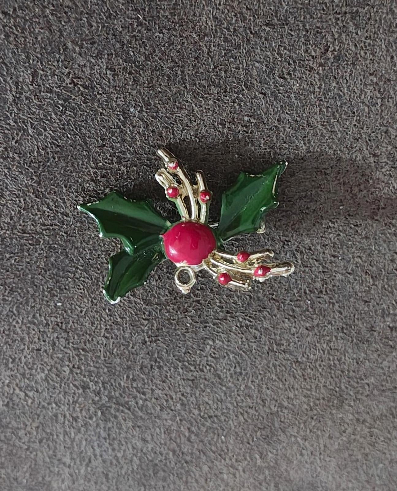 Holly enamel brooch pin on dark fabric: green leaves, red berry center, gold-tone details