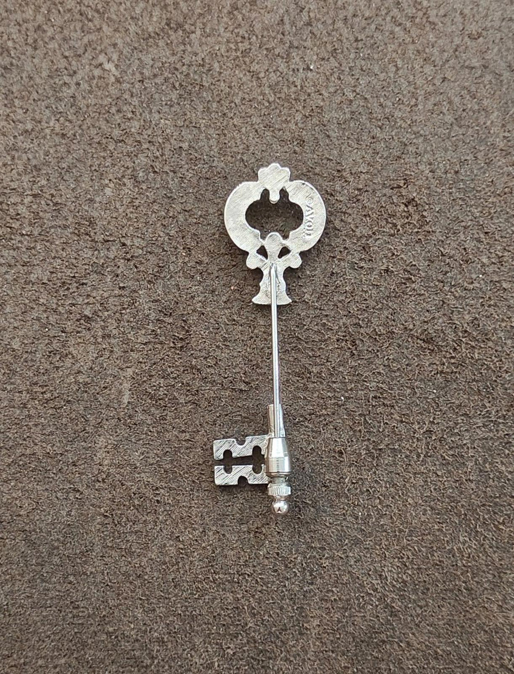 Silver skeleton key stick pin underside view, showing pin stem and key charm.